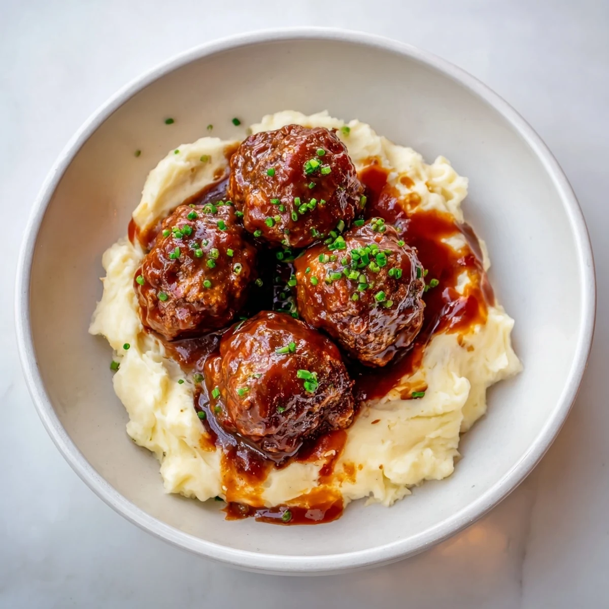 A close-up shot of rich, glossy BBQ Meatballs with creamy mashed potatoes, a comforting classic.