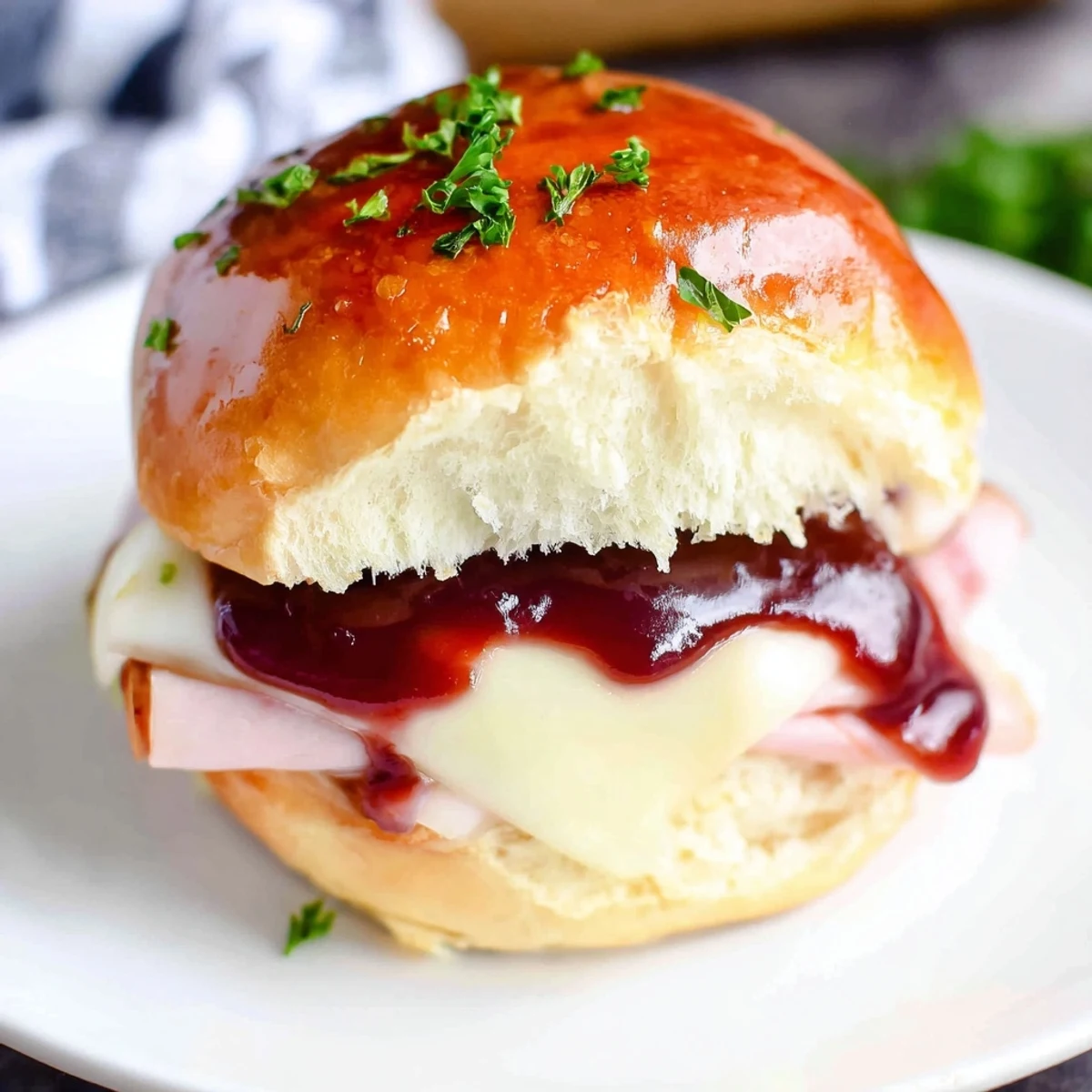 A close-up of Cherry-Glazed Ham and Cheese Slider Mashup, oozing melted cheese and sweet glaze.