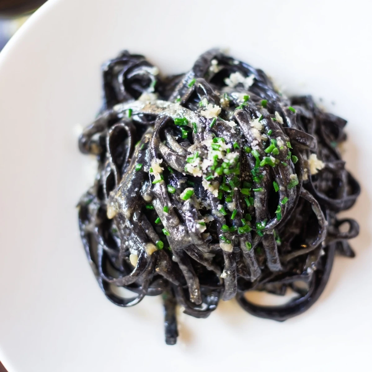 Vibrant Parmesan and chives top the rich cream sauce of this stunning Squid Ink Pasta dish.