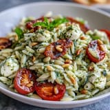 Vibrant orzo pasta salad with fresh basil, sweet cherry tomatoes, and creamy mozzarella, tossed in zesty basil pesto dressing.
