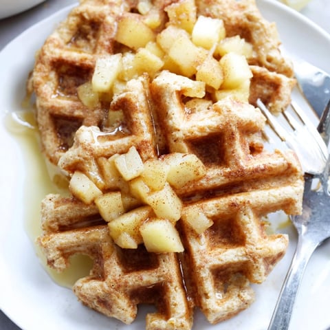 Golden Cinnamon Apple Protein Waffles, warm and fragrant, are drizzled with sweet maple syrup.