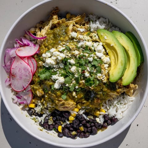 Steaming bowl of Green Enchiladas Rice Bowl, showcasing chicken, rice, beans, and fresh vibrant toppings.