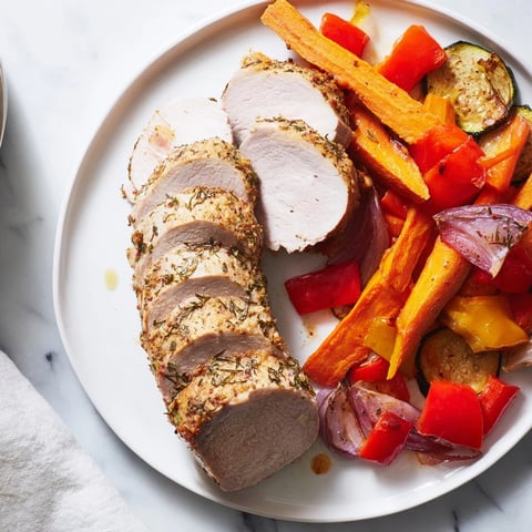 Tender roasted garlic pork tenderloin glistening beside vibrant, caramelized vegetables for a family meal.