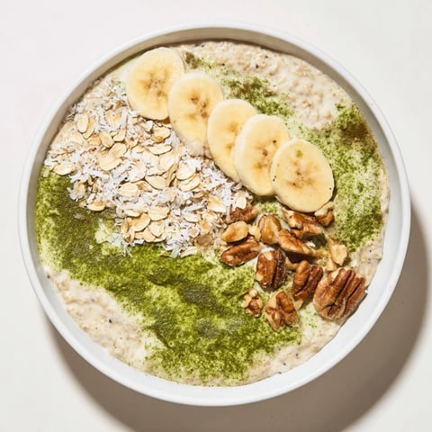 Creamy, green-hued High-Protein Eggnog Matcha Overnight Oats with banana slices sprinkled on top.