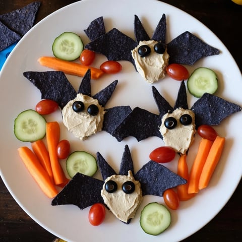 A spooky Halloween Spooky Bat Bean Dip Platter, creamy black bean bats with crunchy chips and colorful veggies.