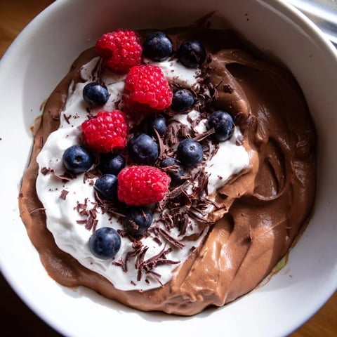 Decadent avocado chocolate pudding in a glass, topped with fresh berries and shaved chocolate.