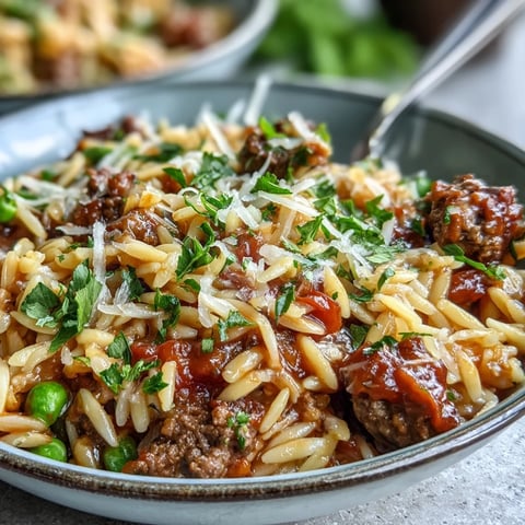A close-up of Comforting Ground Beef Orzo Dinner in a skillet, garnished with parsley and melted Parmesan cheese.