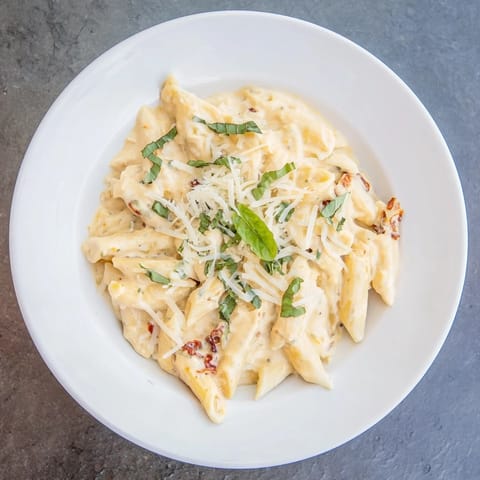 Fresh basil and Parmesan topping a bowl of homemade sun-dried tomato and cottage cheese pasta.