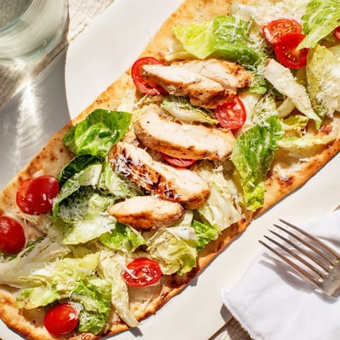 Caesar Chicken Flatbread topped with juicy sliced chicken, fresh greens, Parmesan, and lemon wedges for a vibrant meal.  
