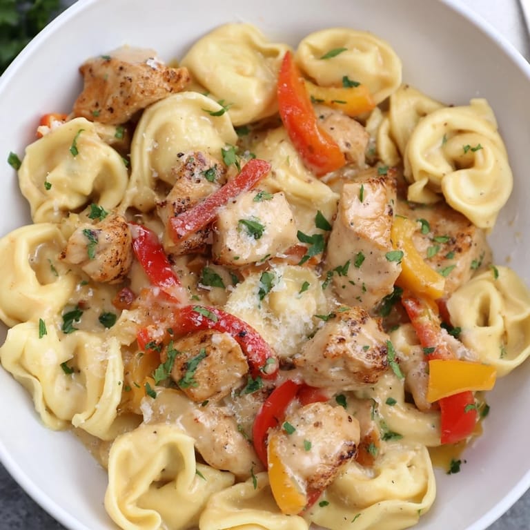 A steaming bowl of Zesty Cajun Garlic Parmesan Chicken Tortellini with parsley garnish and sauce.