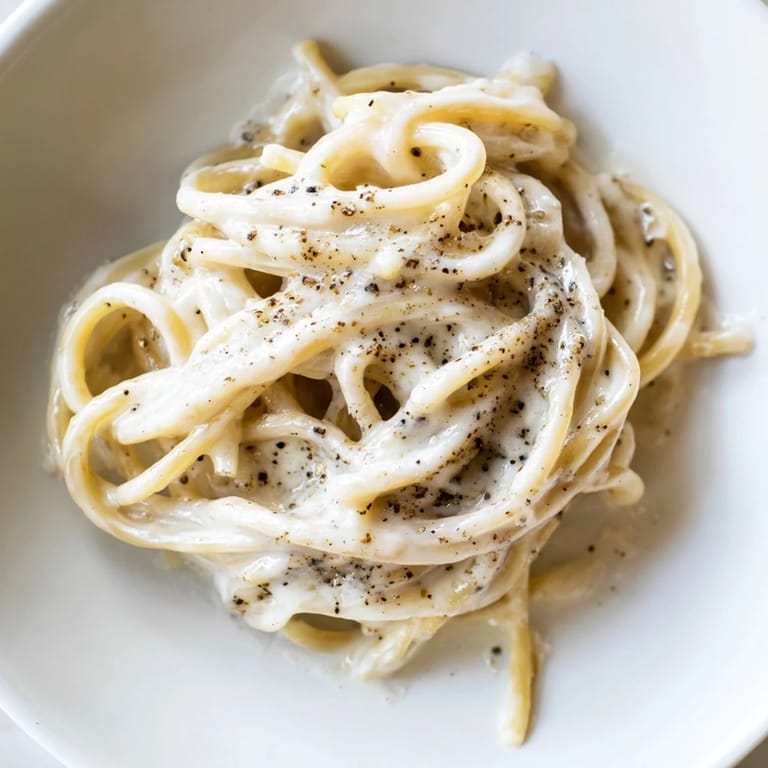 A fork twirls al dente Spaghetti Cacio e Pepe, showcasing the rich, salty cheese sauce and aromatic black pepper.
