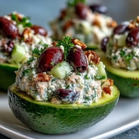 Ripe avocado halves filled with Mediterranean tuna salad, featuring cherry tomatoes, cucumbers, and Kalamata olives.