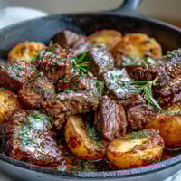 Sizzling steak bites and golden crispy potatoes tossed in a garlic butter sauce in a hot skillet.